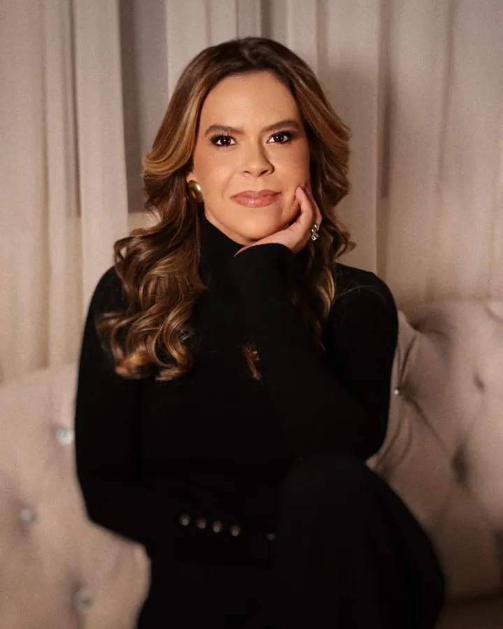 Juliana Bambil sentada em um sofá, com expressão serena e a mão apoiada no rosto.
